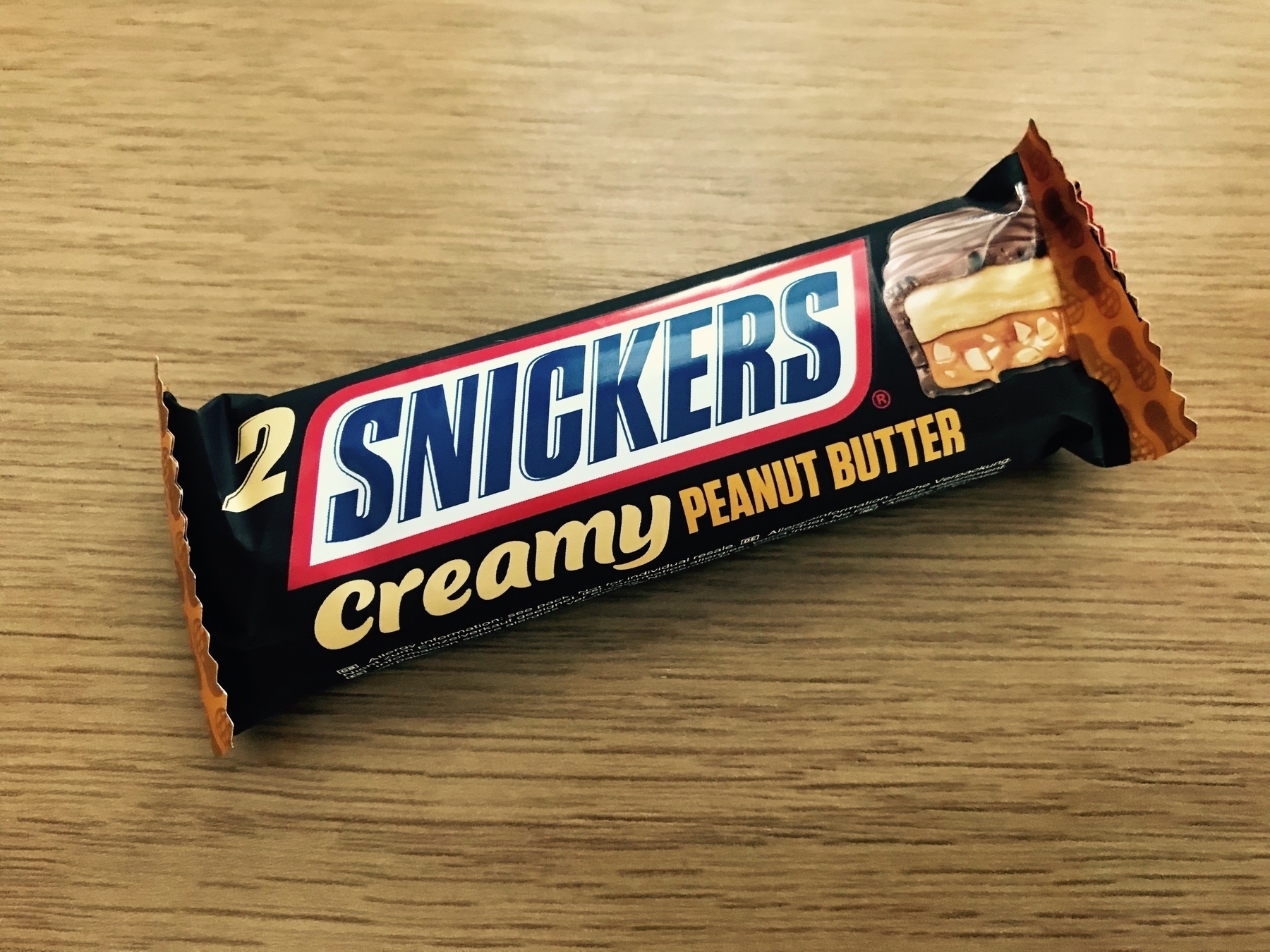 Snickers Creamy Peanut Butter bar on a wood-like kitchen countertop.