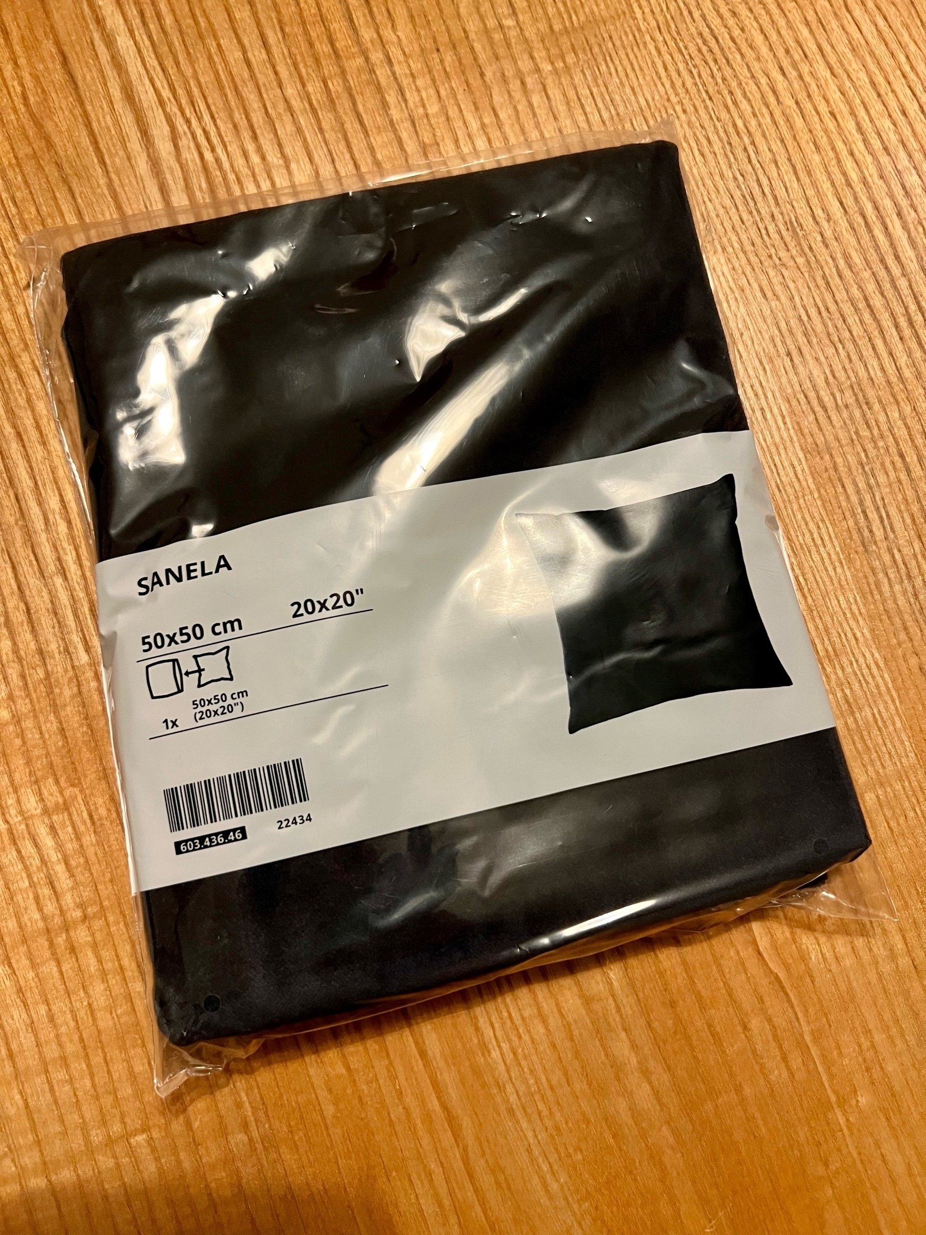 Schwarzer Kissenbezug ”Sanela“ von IKEA in der Verkaufsverpackung auf einem Holztisch.