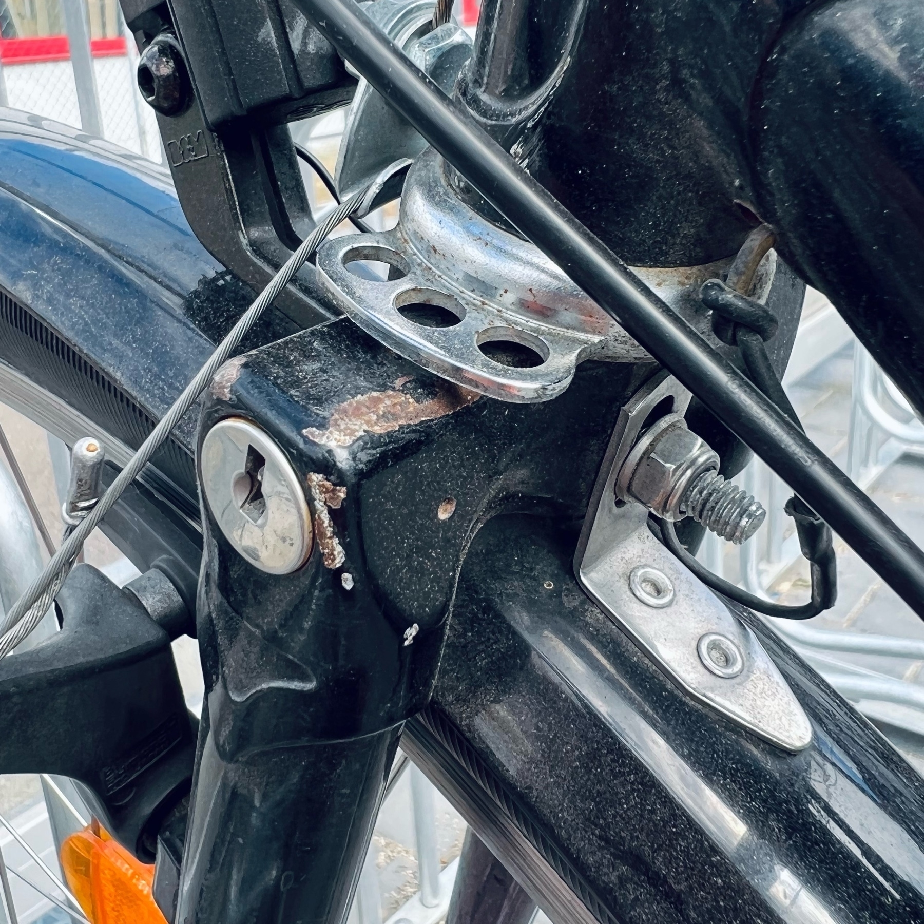 Close-up of the left side of a bicycle fork crown. It has attachment points for a bolt in the form of a plate that's sirting below the steerer tube. A the top of the left fork blade, a lock core is embedded inside the gusset.
