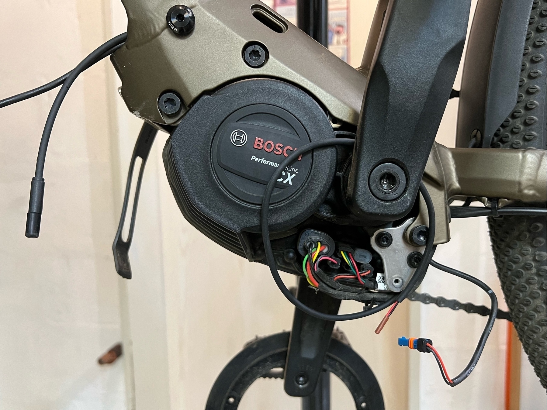 Bosch Performance CX ebike motor unit, surrounding frame, part of the back wheel and exposed, disconnected cables for the headlight. Photographed from the non-drive side.