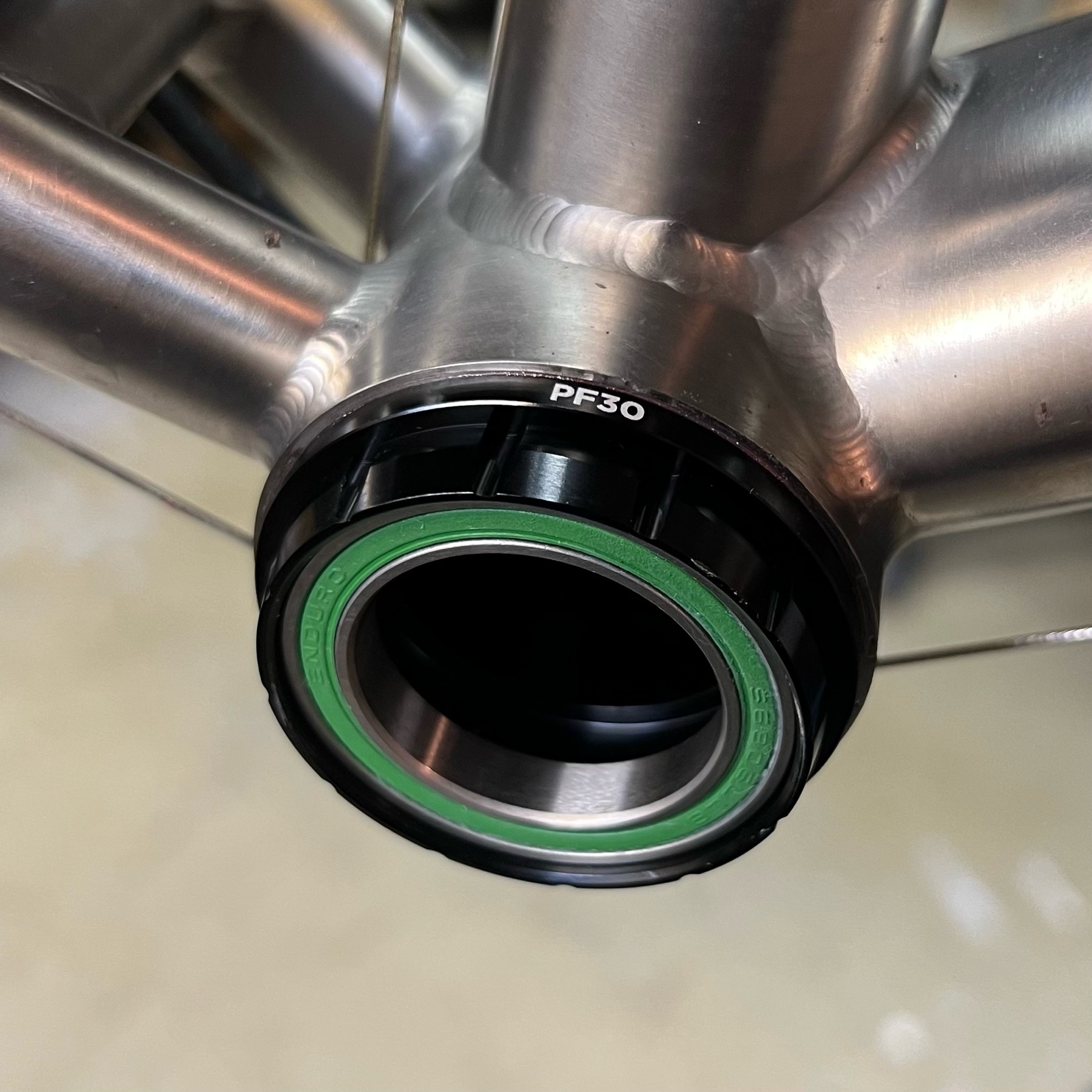 Black-anodised Cane Creek Hellbender 70 bottom bracket in a titanium bicycle frame. The green outer seal of the Enduro bearings are visible.
